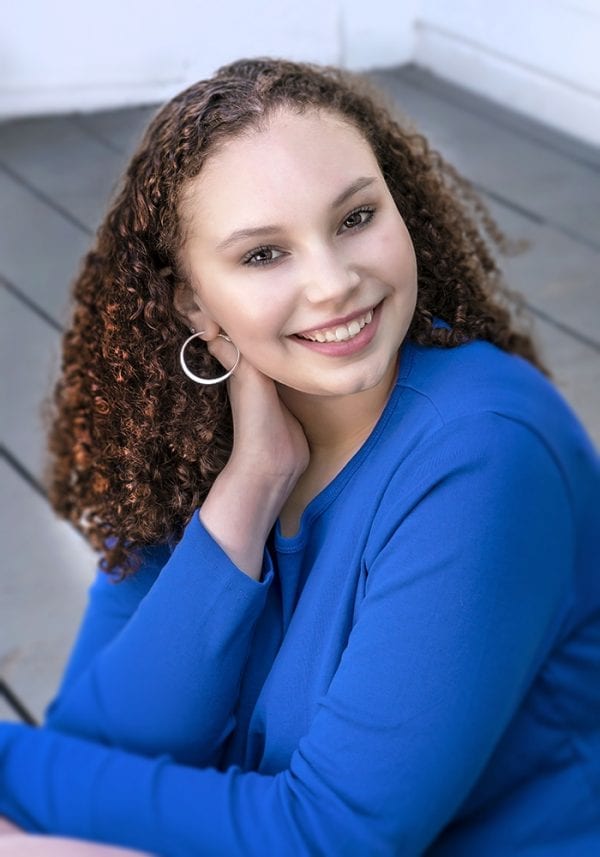 Portrait of a teen girl in a simple blue sweater on a porch