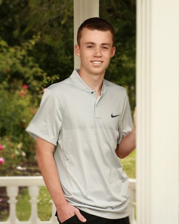 Portrait of a teen boy in a sports polo with his hand braced on a wall