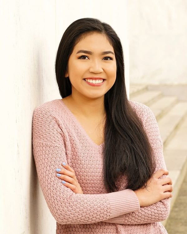 Portrait of a teen girl leaning against a wall in a light pink sweater