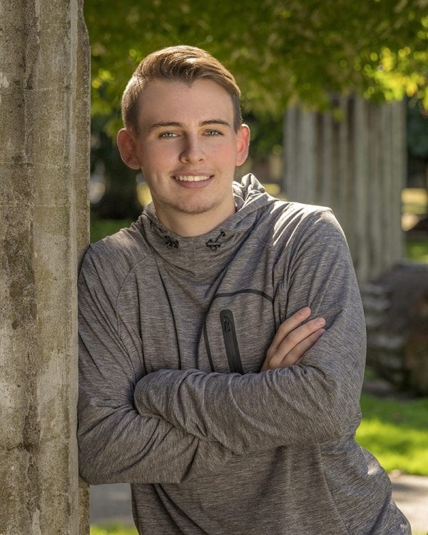 Portrait of a teen boy leaning against a roman column in a gray sports sweatshirt