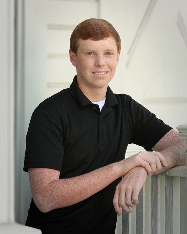 Portrait of a teen boy leaning against a railing in a nice black polo