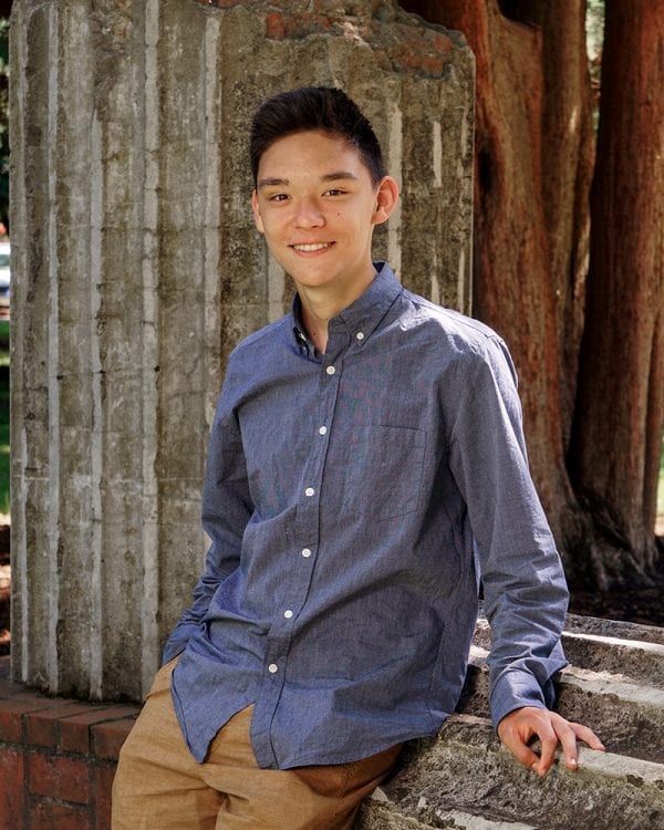 Portrait of a teen boy leaning against a roman column that has fallen over