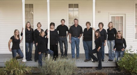 Large family photo all wearing black in front of cream colored house