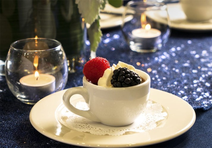 Dessert drink in a mug with a raspberry, blackberry, and dollop of whipped cream on a candlelit table