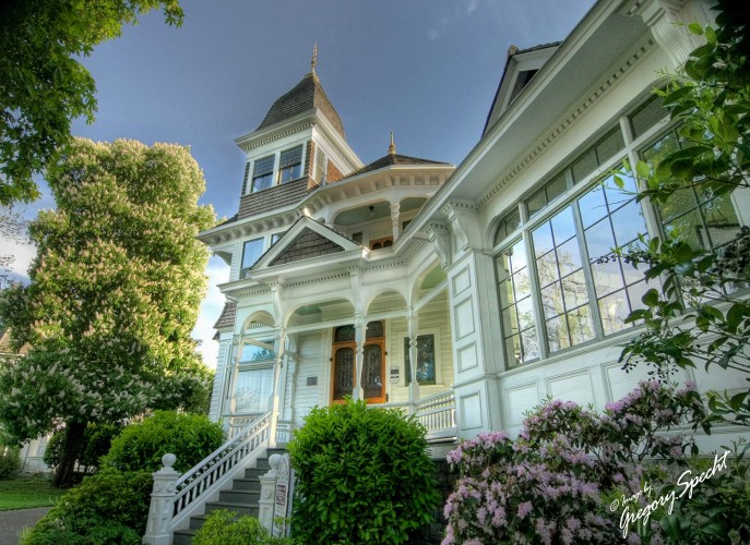 Exterior view of white mansion-style home with beautiful greenery around