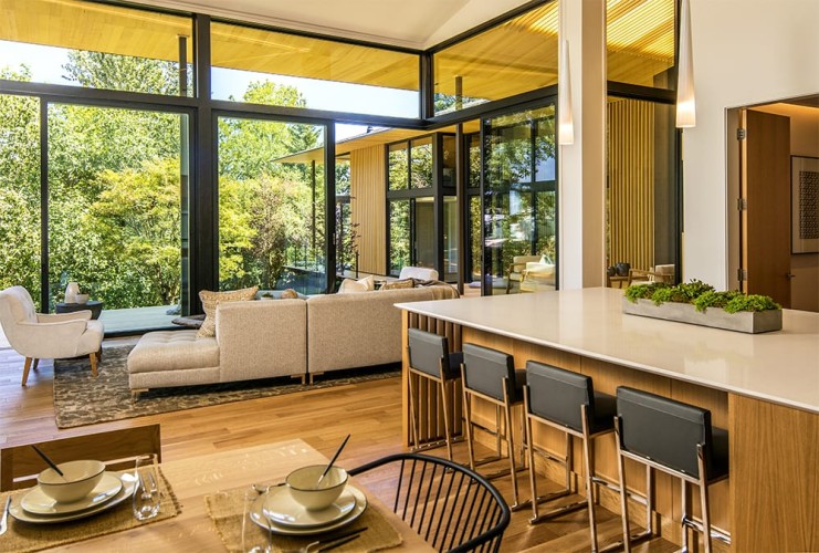 View from kitchen and dining into the living room with a view of the trees outside the floor to ceiling windows