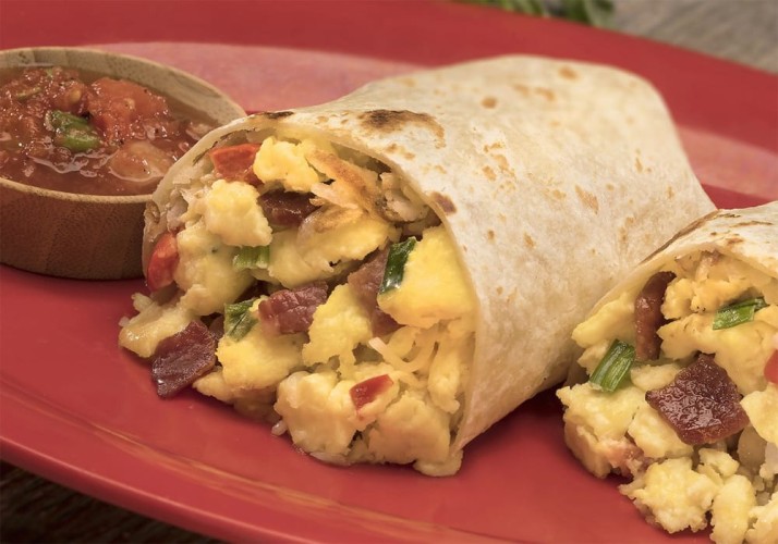 Close up of breakfast burrito overflowing with eggs, bacon, and veggies on a red plate