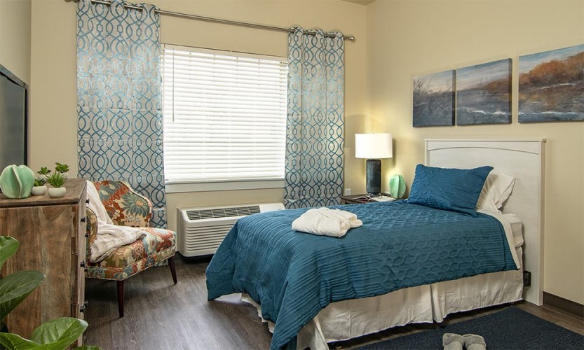 Small bedroom/living space, bed with blue comforter, lake paintings, and other blue/nature themed furnishings