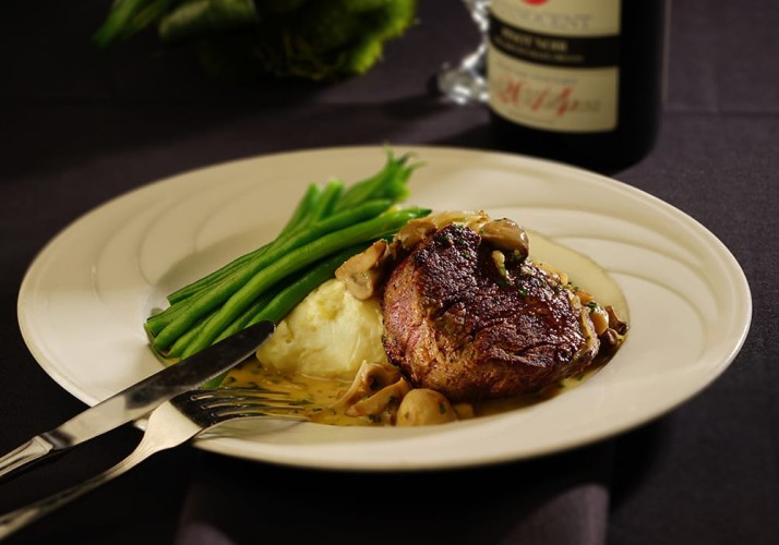 Juicy steak plate with mashed potatoes, string beans, and silverware ready to eat